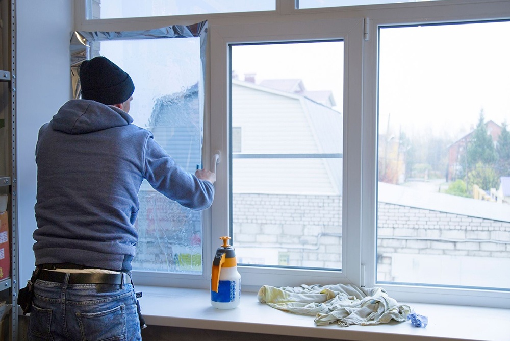 Man installing window film to protect home's windows before a hurricane.